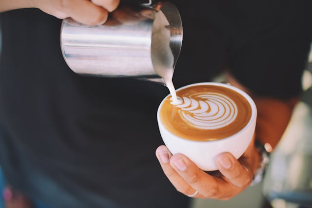 barista pouring milk froth artistically into a hot latte